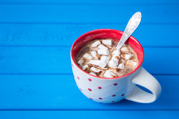 Hot chocolate with marshmallows isolated on blue wooden background.