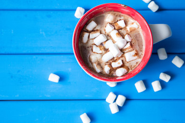 Hot chocolate with marshmallows isolated on blue wooden background.