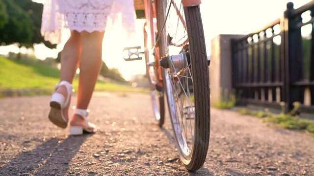 Young beautiful woman walking with a bicycle at sunset. Slow motion