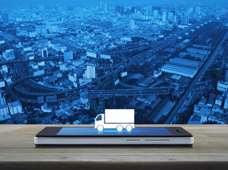 Truck flat icon on modern smart phone screen on wooden table over city tower, street and expressway, Business transportation service concept