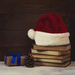 Obraz na płótnie Canvas Santa Claus hat, a gift wrapped with a blue ribbon, a cone, books
