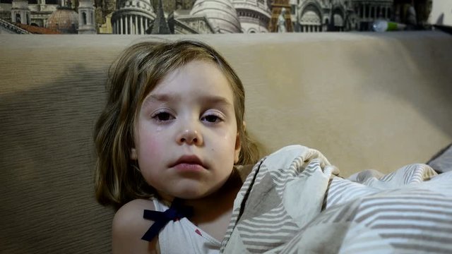 4K footage. A frustrated, tear-stained child in bed. Girl 4-5 years of European appearance. She has tears in her eyes.