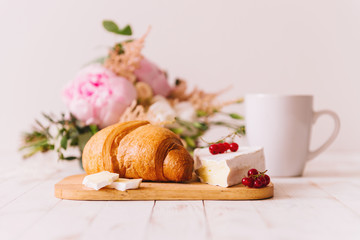 Delicious healthy wholesome breakfast with fresh flaky croissant served on a cutting board with butter, fresh berries and cheese, cup of coffee on white vintage kitchen table.