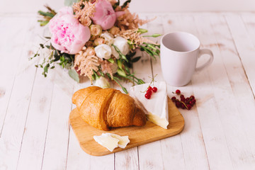 Fototapeta na wymiar Delicious healthy wholesome breakfast with fresh flaky croissant served on a cutting board with butter, fresh berries and cheese, cup of coffee on white vintage kitchen table.