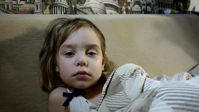 4K footage. A frustrated, tear-stained child in bed. Girl 4-5 years of European appearance. She has tears in her eyes.