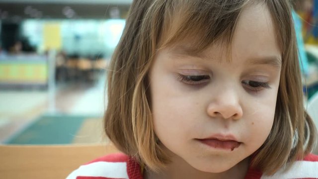4K footage. A European, Russian girl, 4-5 years old, sits on a food court and eats a pancake with chocolate.
