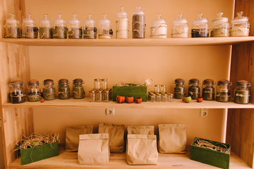 Set of different spices and herbs in glass jars, paper packages on wooden shelves, racks. Healthy food ingredients - choice of herbs, seeds. Curry, saffron, turmeric, pepper, salt and rosemary.