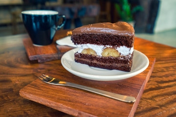 Chocolate Fudge with white cream and banana on white plate and hot coffee background on wooden table.