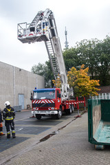 Red european fire truck, three-quarter frontal view, with the long ladder extended.