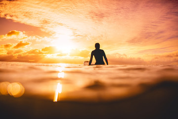 Surfer woman in ocean at sunset or sunrise. Winter surfing in ocean