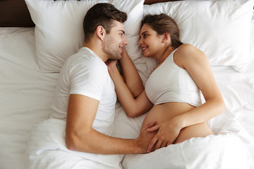 Cheerful pregnant woman lies in bed with husband
