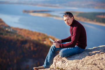 Fototapeta na wymiar a man sits on top of a mountain, admires the scenery and works on a tablet
