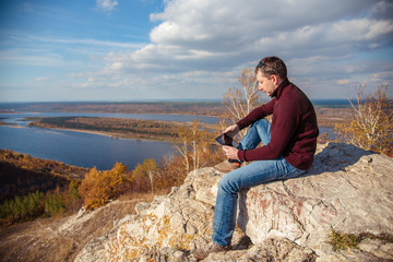 a man sits on top of a mountain, admires the scenery and works on a tablet