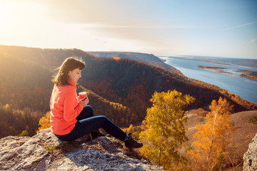 Naklejka premium the girl is drinking tea on top of the mountain, holding a mug in her hands