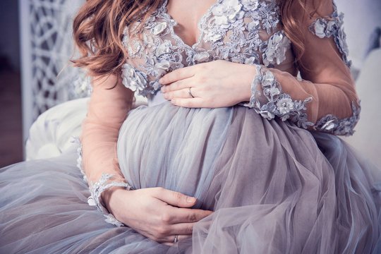 Beautiful pregnant girl in luxurious dress, holding her hands belly. Closeup female belly