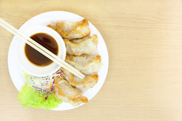 Top view of Fried Gyoza, Japanese dish consisting of wonton wrappers stuffed with pork and cabbage on white dish, eat with soy sauce, on wood table, have copy space