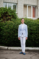 Portrait of a fashionable and stylish high school graduate in elegant tuxedo posing outdoor with bushes on the background.