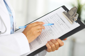 Close-up of a female doctor filling  up medical form at clipboard while standing straight in hospital
