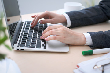 Close-up of business woman  hands  typing on  laptop computer in the white colored office.