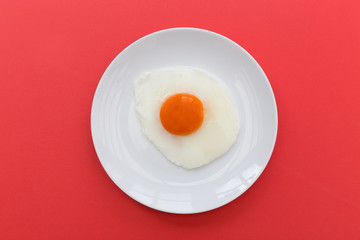 Fried egg and yoke overhead on plate and red background