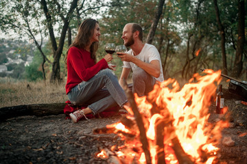 Enamored couple sits and smiles on picnic in forest on bonfire flame background.