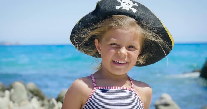 Little happy girl in a pirate hat is playing at the sea looking in a telescope, a background of sea blue water.
