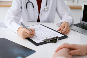 Close up of a female doctor filling up  an application form while consulting patient