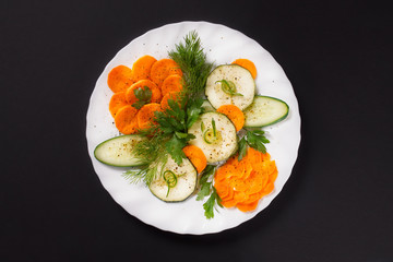 Festive cutting from fresh vegetables with greens and black pepper on a white plate on a black background.