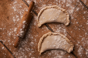 Uncooked chebureki with flour in wooden bowl