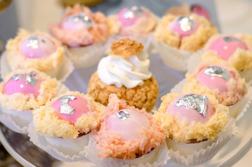 Delicious wedding reception glaze pink candy sweet desserts cakes on glass plate with edible flaked leaf of silver. Candy bar dessert.