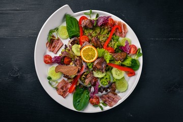 Salad with bacon and chicken liver. On a wooden surface. Top view. Free space for your text.
