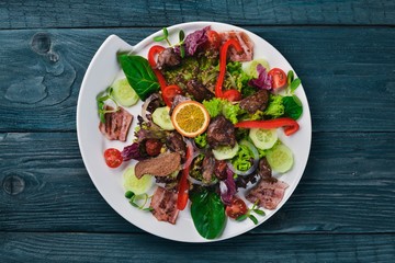 Salad with bacon and chicken liver. On a wooden surface. Top view. Free space for your text.