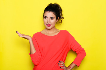 Beautiful woman presenting something with hand. Studio shot on yellow screen.