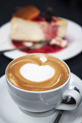 Cup of cappuccino coffee and piece of cheesecake  on the table
