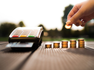 Hand putting money coins stack growing and credit cards swipe through terminal on nature...