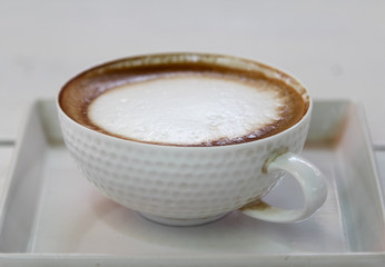 Hot cappuccino on white tray in morning time.