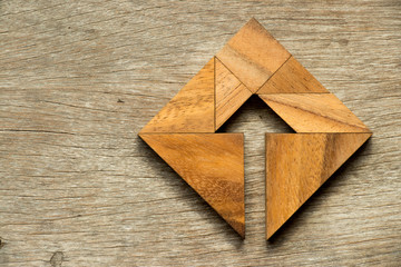 Tangram puzzle in square shape with the arrow symbol inside on wood background