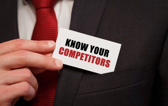 Businessman putting a card with text KNOW YOUR COMPETITORS in the pocket