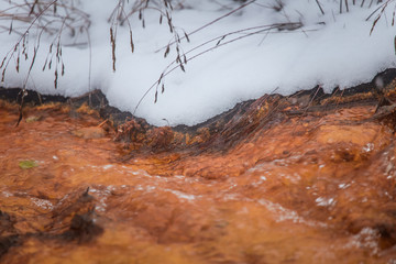 An orange rusty water at the old copper mine in Norway in winter. Bright color stream details, closeup.