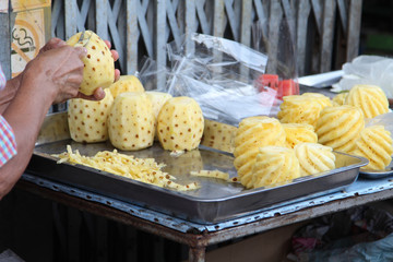 Male's hands peeling pineapple fruit then put it on the stainless steel tray.