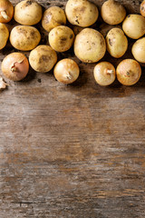 Raw whole organic potatoes with soil, onion, garlic over old wooden background. Top view with copy space