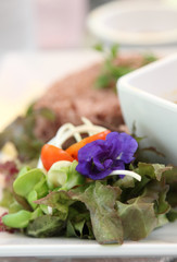 Salad with pea flower on white plate.