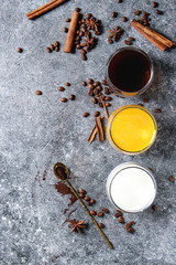 Ingredients for cook spicy pumpkin latte. Glasses with black coffee, pumpkin milk, cream with spices, coffee beans and decorative pumpkins above over gray texture background. Top view, space.