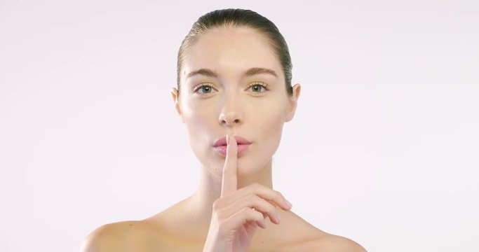 Close up of the face of a beautiful girl with perfect skin and clean from all impurities and with her finger in front of her mouth it is a sign of silence. Concept of beauty secrets and creams.