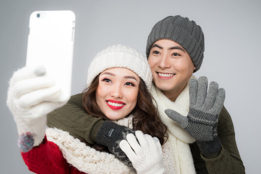 Happy couple in their winter clothes taking picture with smartphone
