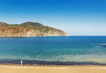Small woman silhouette on a wild beach in solitary bay in mediterranean sea