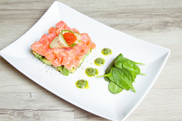 Tartare from salmon, caviar and avocado with pesto sauce and spinach. Close-up, selective focus.