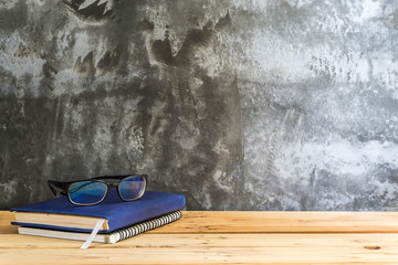 wooden table with diary book, black glasses and pen on modern loft cement wall background