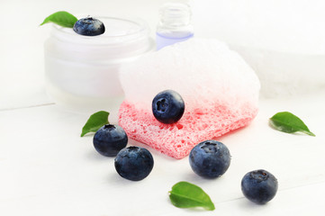 Blueberry facial wash. White soap foam with fresh berries, cleansing cosmetic product, pink sponge, light background.