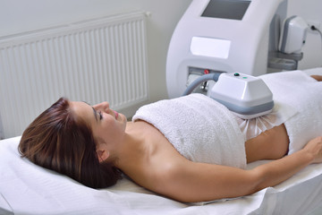 Beautiful young woman getting cryolipolyse treatment in cosmetic cabinet